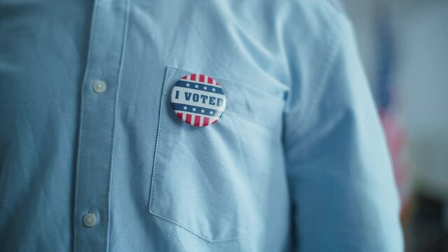 Close up of anonymous man or male voter putting on badge with American flag logo and inscription I Voted. US citizen at polling station during elections. National Election Day in the United States.