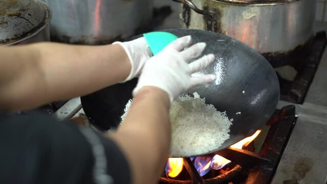 Close up of Chef hands cooking and thowing white rice for Asian cuisine in frying wok pan on gas stove.
