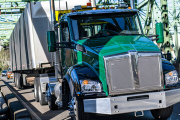 Bright green day cab big rig semi truck transporting cargo in tented dry van semi trailer driving on the truss bridge at sunny day