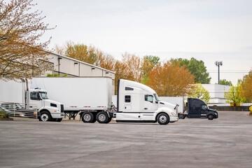 Different big rig semi trucks with dry van semi trailers standing in warehouse dock gaits