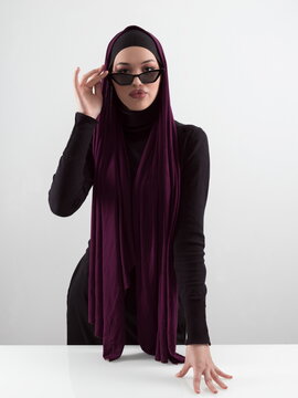 Portrait of beautiful stylish young muslim woman wearing black hijab and sunglasses as modern eastern fashion concept posing on white background.