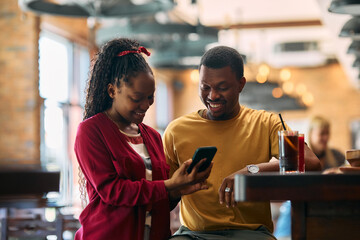 Happy black couple using app on mobile phone in  bar.