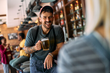 Cheerful man drinking beer while talking to his friend in pub.