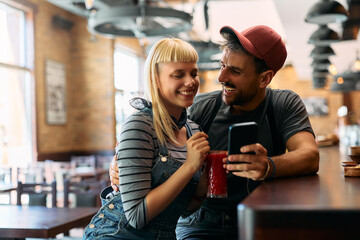 Young couple having fun while using smart phone in  bar.