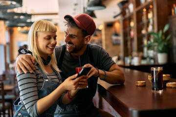 Cheerful man and his girlfriend using mobile phone in  pub.