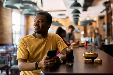 Smiling black man text messaging on cell phone in  pub.