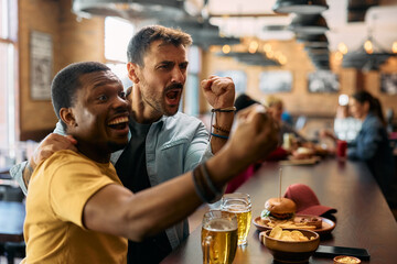 Cheerful men cheering for their team while watching sports game in man pub.