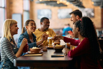 Young happy woman eating with friends in  pub.