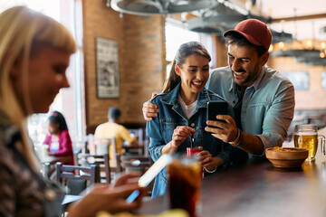 Young couple having fun while using cell phone in bar.