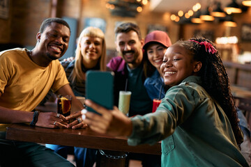 Happy black woman taking selfie with her friends in bar.