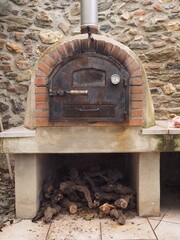 Old, rusty wood-fired oven with a closed door and firewood