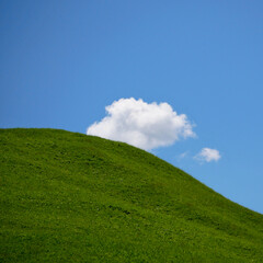 single cloud in beautiful weather over a green hill