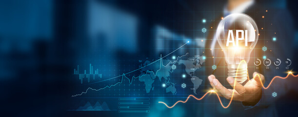 Businessman holding a creative light bulb with a growth graph and API icons. Harnessing API innovation technology to develop new applications and solutions that enhance success and profitability.