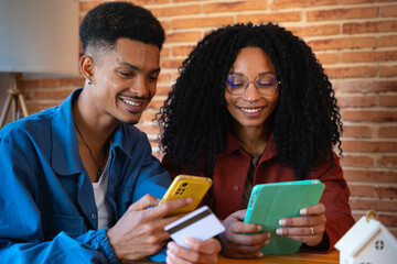 Multiracial smiling Young Couple Sitting On the table Happy Entering Credit Card Number On Tablet...
