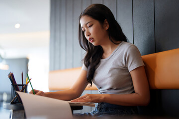 Asian teenage student woman using color pencil to highlight data in paperwork and taking notes while reading a book to studying and learning about education knowledge for preparing test exam in cafe - 788990811