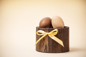 multi-colored chicken eggs for Easter in a wooden basket on a beige background.