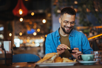 Portrait of a happy man eating at a restaurant and smiling - lifestyle concept. A young man with a beard sitting in a restaurant and holding hands french fries and going to eat - 788996856