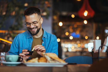 Portrait of a happy man eating at a restaurant and smiling - lifestyle concept. A young man with a beard sitting in a restaurant and holding hands french fries and going to eat - 788997041