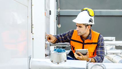 Male technical foreman in safety uniform inspects maintenance work holding a tablet to look at plumbing and electrical systems on the roof of a building, Technician man worker checking power system