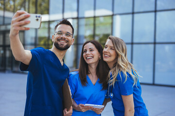 Cheerful medical students taking selfie and having fun at the university. Close up of Diverse medicine students in uniform taking selfie in front of Hospital. To remember our medical internship - 789005402