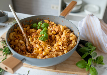 Delicious tuna pasta pan with cheese and basil garnish on kitchen table