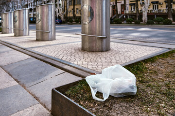 A bag of garbage lies on the lawn on the sidewalk in the city