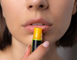 portrait of young woman using natural ingredients home made lip balm and cream.girl applying on lips and cheeks.facial cosmetic from oils, lemon and cocoa butter.smiling female holding bottle on face.
