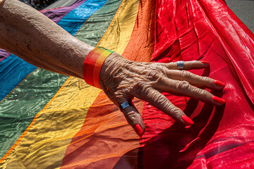 Hand of an elderly person touching a rainbow flag on the street
