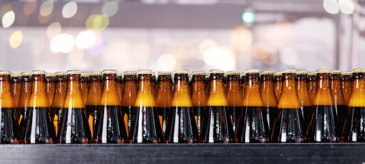 Detailed view of sealed beer bottles on production line with sun light. Industry brewery plant