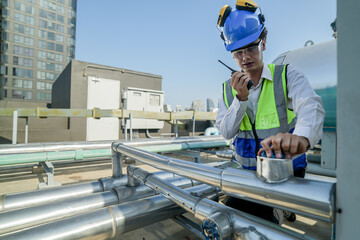 Service engineer in protective gear working on heating and cooling systems atop a city building, surrounded by metallic ductwork under the midday sun