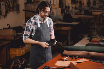 Portrait happy tailor working with natural brown leather in workshop. Small business of shoemaker...