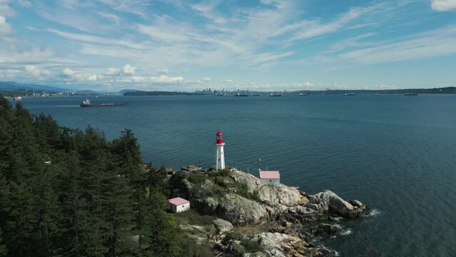 aerial view tilting down point atkinson lighthouse in lighthouse park near vancouver city on an sunny day with some clouds in British Columbia, Canada