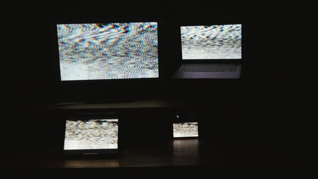 Four digital computer device screens flashing a strobing static noise pattern in a dark room.
