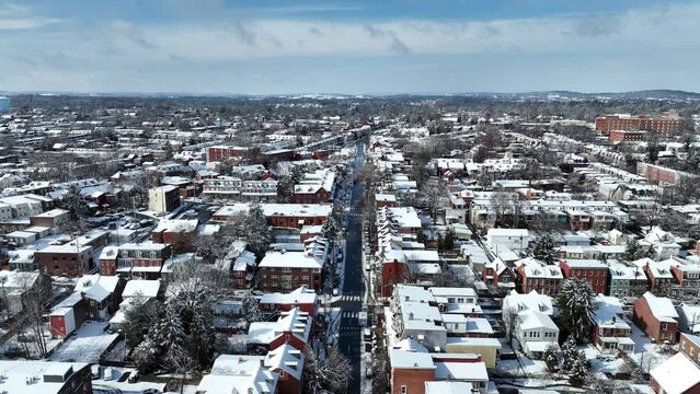 Aerial view of a snow-covered American cityscape with rows of houses and road. Aerial truck shot on sunny winter day.