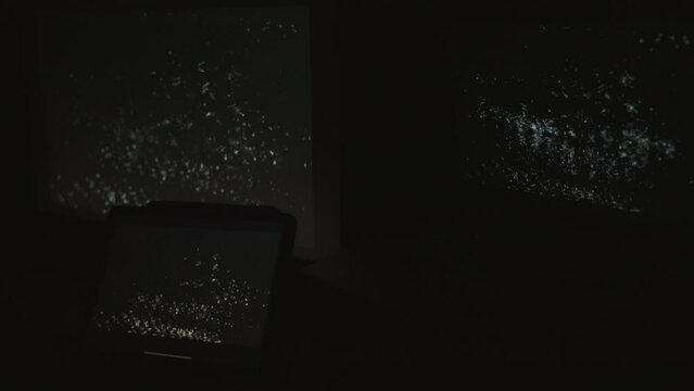 Tight shot of three digital computer devices flashing a strobing static noise signal in a dark room.