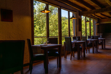 Rustic restaurant room of a mountain hotel, with large windows overlooking the forest and the...