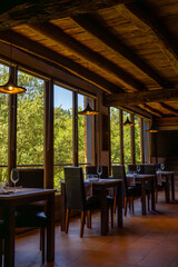 Rustic restaurant room of a mountain hotel, with large windows overlooking the forest and the...