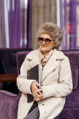 An elderly woman with a laptop in her hands on a purple background.
