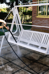 Female's hand cleaning a white garden rocking chair with a pressurized water machine in the...
