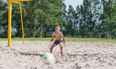 A little boy is playing soccer on the sand - obrazy, fototapety, plakaty
