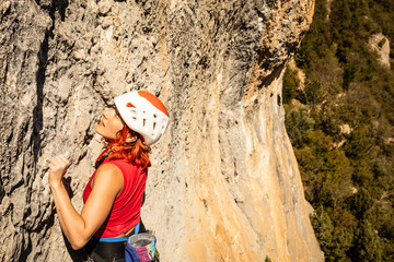 A woman in a red shirt and red hat is climbing a rock wall - obrazy, fototapety, plakaty