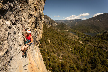 A woman is climbing a rock wall with a red jacket - obrazy, fototapety, plakaty