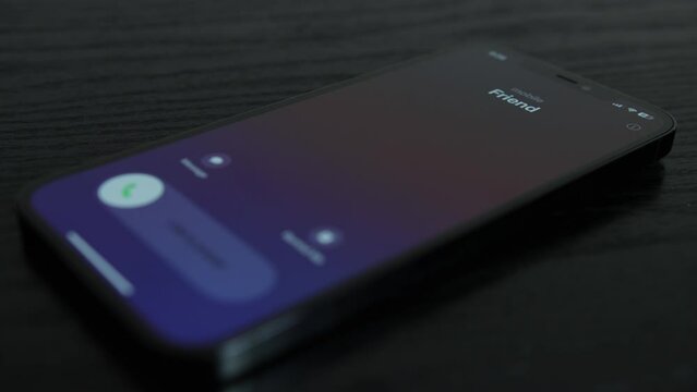 Close-up shot of an iPhone receiving a call from a friend on black wooden table