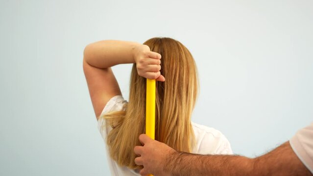Blonde woman doing shoulder mobility exercise with stick supervised by physiotherapist