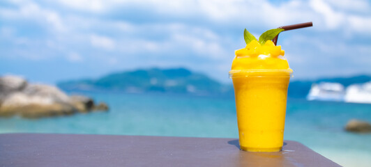 Smoothie made from fresh mango fruits against the backdrop of a seascape. Fruit and yoghurt ice cream decorated with leaves. Glass of tropical dessert close-up.