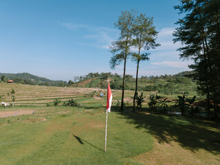 Indonesian flag waving proudly against a backdrop of fields, rice paddies, and lush trees, symbolizing national pride and natural beauty.