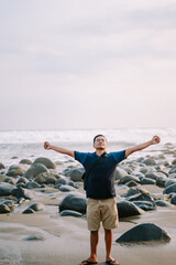 A contented man in a blue tee and shorts stands by the shore, his gaze fixed towards the horizon, radiating happiness against the backdrop of the beach