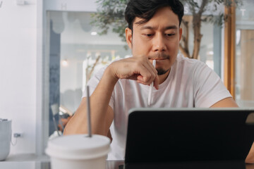 Front view of asian man using laptop, sitting and working at cafe. digital nomad and freelance concept.