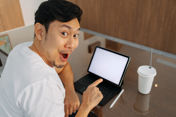 Asian man wow shocked face, pointing finger to white blank screen on laptop, presenting some good idea, great choice, working and sitting in cafe.