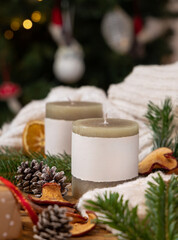 Pillar candles with label near Christmas decor, sweater and fir twigs, cozy winter mockup
